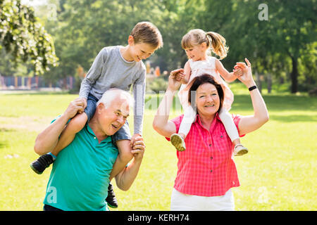 Glückliche Großeltern, die Spaß piggyback Fahrt zu ihrem Enkel in Park Stockfoto