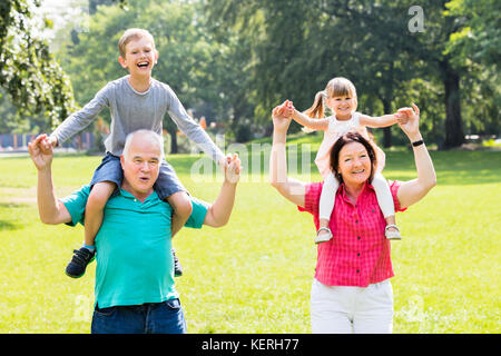 Glückliche Familie Spaß mit Kinder piggyback Ride in Park Stockfoto