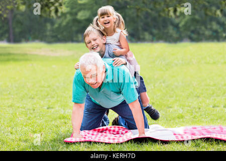 Gerne ältere Großvater mit zwei Kindern liegen auf Gras im Park Stockfoto