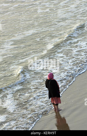 Eine ältere oder im mittleren Alter asiatischen oder indischen Lady oder Frau im Meer paddeln auf der Isle of Wight am Meer. Stockfoto