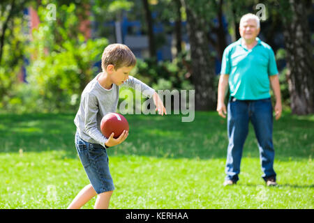 Kid wirft Rugby Ball zu Großvater beim Spielen im Park Stockfoto