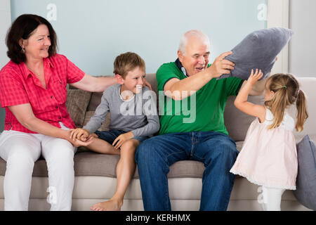 Ältere glückliche Großeltern in Kissen mit Kindern auf der Couch Kampf gemeinsam zu Hause Stockfoto