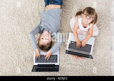 Hohe Betrachtungswinkel von Kindern mit Laptop auf dem Teppich zu Hause Stockfoto