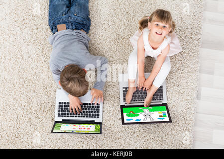 Zwei Kinder mit einem Laptop auf dem Teppich zu Hause Stockfoto