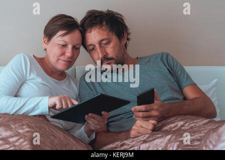 Glückliches Paar, Mann und Frau im Schlafzimmer über elektronische Geräte Stockfoto