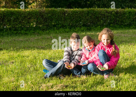 Drei Jugendliche sitzen sie auf dem Rasen spielen in Spinner Stockfoto
