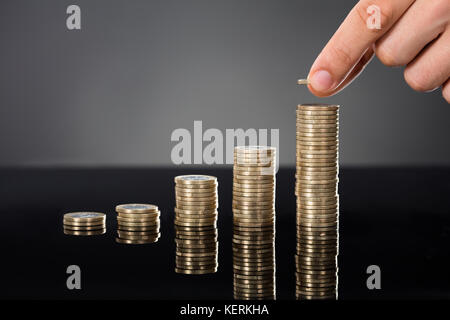 Nahaufnahme einer Person stapeln Münzen am Schreibtisch über grauen Hintergrund. Das Wachstum der Investitionen Konzept Stockfoto