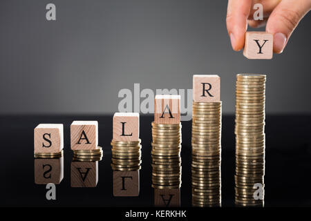 Eine Person, die Hände, die Buchstaben des Wortes Gehalt auf Stapel von Münzen über grauer Hintergrund Stockfoto