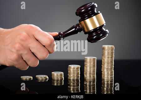 Nahaufnahme eines Richters Hände schlagen Hammer vor gestapelte Münzen am Schreibtisch Stockfoto