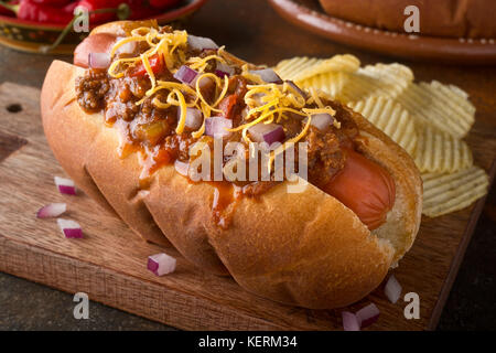 Eine köstliche hausgemachte Chili Hot Dog mit roten Zwiebeln und Cheddar Käse mit Kartoffelchips. Stockfoto