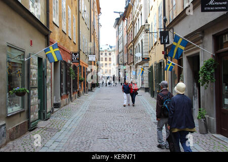 Schmale kleine touristische Straße in der Altstadt Gamla Stan. Zentrum des skandinavischen Stadt mit gemütlichen Cafes, Souvenirläden und Fußgänger. hung Flags Stockfoto