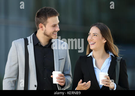 Glückliches Paar von Führungskräften zu Fuß in Richtung Kamera und Konversation auf der Straße mit einem Bürogebäude im Hintergrund Stockfoto