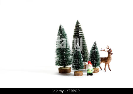 Isolierte Gruppe der vollen künstliche Tannen wie ein kleiner Wald Baum in einem keramischen Muster Platte mit einer Figur Rentiere und Gartenzwerg neben auf einem weißen Stockfoto