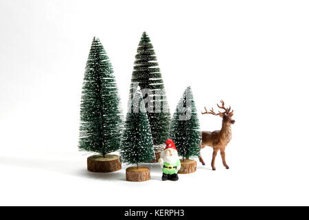 Isolierte Gruppe der vollen künstliche Tannen wie ein kleiner Wald Baum in einem keramischen Muster Platte mit einer Figur Rentiere und Gartenzwerg neben auf einem weißen Stockfoto