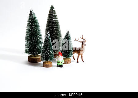 Isolierte Gruppe der vollen künstliche Tannen wie ein kleiner Wald Baum in einem keramischen Muster Platte mit einer Figur Rentiere und Gartenzwerg neben auf einem weißen Stockfoto