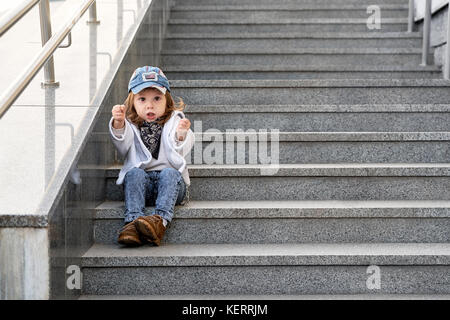 Modell Kind hip-hop sitzen auf der Treppe im Freien. Mädchen Street fashion jeans Kleidung Stockfoto