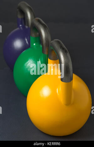 Gelb, Grün und Violett Wettbewerb kettlebells stellten sich in einer Reihe auf ein Krafttraining gym Boden Stockfoto