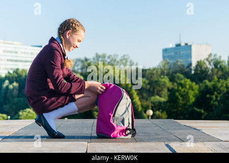 Mädchen in Schuluniform öffnet ein rosa Rucksack für Lehrbücher Stockfoto
