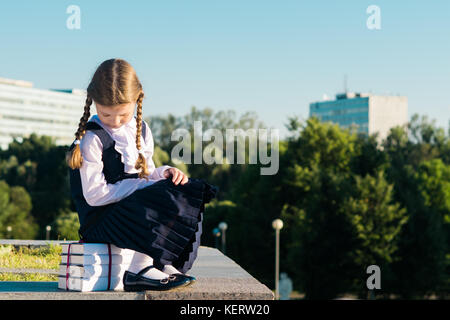 Kleines Schulmädchen sitzt auf einem Lehrbuch für die Schule Stockfoto