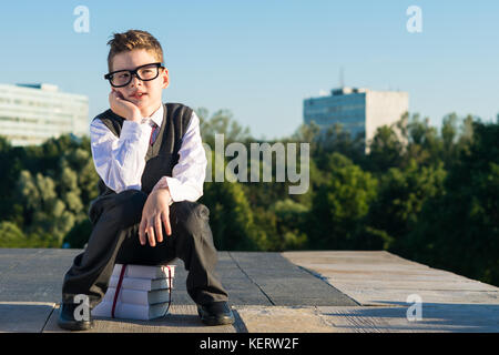 Der Junge aus der Schule in Gläsern sitzt auf Lehrbücher Stockfoto