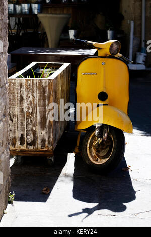 Eine alte, handbemalte, gelbe vespa-Motorroller parkte auf dem Bürgersteig und war unbeaufsichtigt Stockfoto