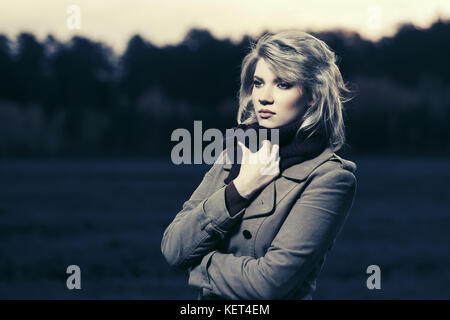 Traurige junge blonde Frau im Classic Mode Mantel wandern Outdoor Stockfoto