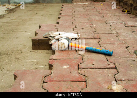 Festlegung der Pflastersteine durch Mosaik Nahaufnahme. Straße pflastern, Bau. Arbeitnehmer Festlegung Stein Pflasterung Platte. mit farbigen Fliesen in einem Stadtpark. Stockfoto