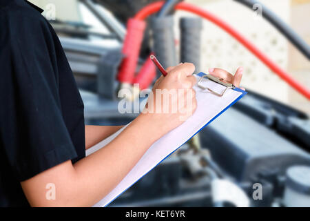 Portrait von lächelnden jungen Mechanikerin Inspektion auf ein Auto in Werkstatt Stockfoto