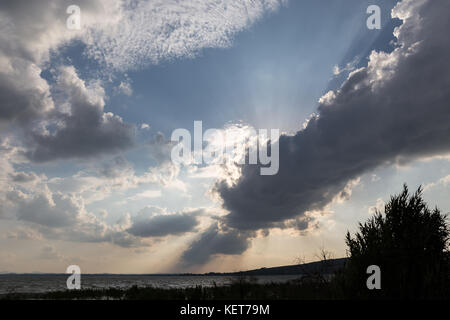 Leistungsstarke Sonnenstrahlen, die sich durch einige Wolken über einem See Stockfoto