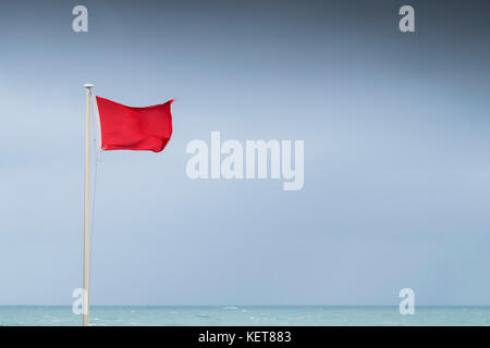 Rote Fahne - eine rote Flagge in High Wind am Fistral Beach Newquay Cornwall fliegen. Stockfoto