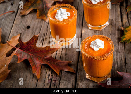 Herbst trinken. Ideen und Rezepte für Danksagung, Halloween. Alkohol cocktail Kürbistorte Wodka Schüsse auf alten rustikalen Holztisch mit Herbstlaub, Co Stockfoto