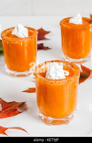 Herbst trinken. Ideen und Rezepte für Danksagung, Halloween. Alkohol cocktail Kürbistorte Wodka Schüsse auf weißem Marmor tisch mit Herbstlaub, Kopieren sp Stockfoto