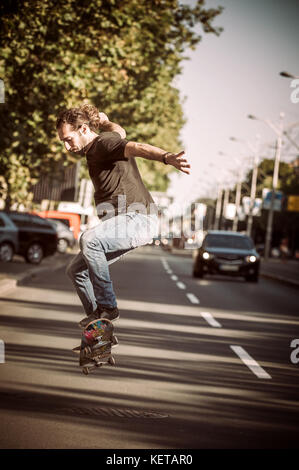 Pro Skater Reiten Skate, macht Tricks und Sprünge auf den Hauptstraßen durch Autos und Stadtverkehr. Free Ride Skateboard Stockfoto