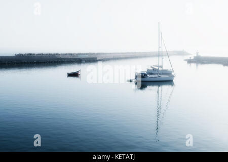 Zwei Segelboote (Yachten) und ein kleines Motorboot am frühen Morgen verankert. high key Bild mit Soft Focus und Glühen. Stockfoto