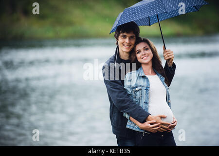 Schwangere Frau und Mann hält ein Regenschirm im Park in der verregneten Tag im Freien. Stockfoto