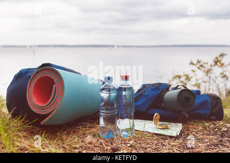 Eine Reihe von touristischen notwendigen Zubehör für den Tourismus in der wild. Mineralwasser, Teppiche, Rucksäcke, Karte und Kompass auf dem Gras im Wald an der Stockfoto