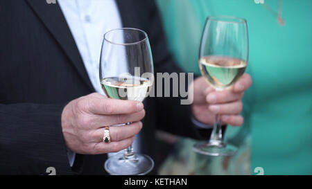 Nahaufnahme eines kaukasischen Mannes in schwarzem Anzug und weißem Hemd, der zwei große Gläser mit Weißwein hält. Großaufnahme von zwei Gläsern Champagner auf Tablett mit Holding b Stockfoto