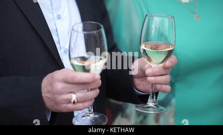Nahaufnahme eines kaukasischen Mannes in schwarzem Anzug und weißem Hemd, der zwei große Gläser mit Weißwein hält. Großaufnahme von zwei Gläsern Champagner auf Tablett mit Holding b Stockfoto