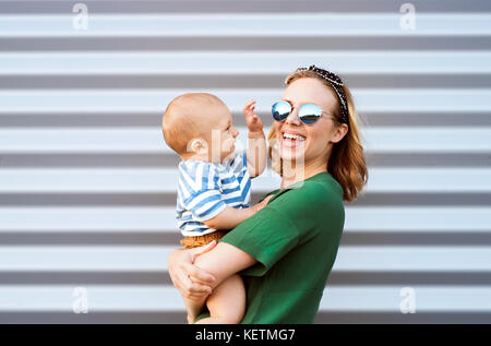 Junge Frau mit einem Baby Junge gegen die Wand. Stockfoto