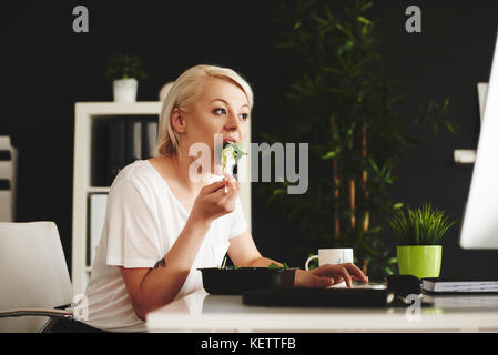 Multipurpose Frau essen und mit einem Computer im Büro Stockfoto