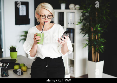 Frau trinkt Gemüsesaft und mobilephone Stockfoto