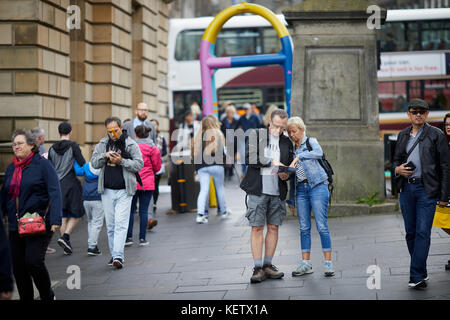 Edinburgh, Schottland, die Royal Mile Canongate verloren Touristen auf einer Karte in der Nähe einer gemalten Security Barrier suchen Stockfoto