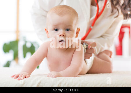 Kinderarzt untersucht neugeborenes Baby. Arzt mit einem Stethoskop, das Kind zurück zu überprüfen Herzschlag zu hören. Kid ist mit Blick auf die Kamera. Stockfoto