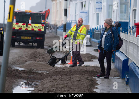 Aberystwyth Wales uk, uk Wetter Montag, 23. Oktober 2017: Nach dem Sturm Winde und wilden Meere der Sturm Brian, lokale Behörde Rat Arbeitnehmer und Auftragnehmer mit Jcb und Bürsten beginnen den Prozess der Clearing die hunderte von Tonnen von Sand und Kies auf die Promenade und das Meer in Aberystwyth gewaschen auf der Cardigan Bay Küste von West Wales. Sie erwarten, dass die Straße für den Verkehr zu haben wieder durch den Nachmittag Foto: Keith Morris/alamy leben Nachrichten Stockfoto