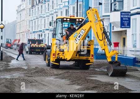 Aberystwyth Wales Vereinigtes Königreich, Montag, 23. Oktober 2017 Vereinigtes Königreich Wetter: Nach dem Sturm Wind und wilde Meere des Sturms Brian, Mitarbeiter des gemeinderats und Auftragnehmer, die JCB's und Bürsten verwenden, beginnen mit der Reinigung der Hunderte Tonnen von Sandsand und Kies, die an der Promenade und am Meer in Aberystwyth an der Küste von Cardigan Bay in westwales angespült wurden. Sie erwarten, dass die Straße bis zum Nachmittag wieder für den Verkehr freigegeben wird. Foto: Keith Morris/Alamy Live News Stockfoto