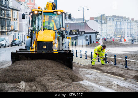 Aberystwyth Wales Vereinigtes Königreich, Montag, 23. Oktober 2017 Vereinigtes Königreich Wetter: Nach dem Sturm Wind und wilde Meere des Sturms Brian, Mitarbeiter des gemeinderats und Auftragnehmer, die JCB's und Bürsten verwenden, beginnen mit der Reinigung der Hunderte Tonnen von Sandsand und Kies, die an der Promenade und am Meer in Aberystwyth an der Küste von Cardigan Bay in westwales angespült wurden. Sie erwarten, dass die Straße bis zum Nachmittag wieder für den Verkehr freigegeben wird. Foto: Keith Morris/Alamy Live News Stockfoto