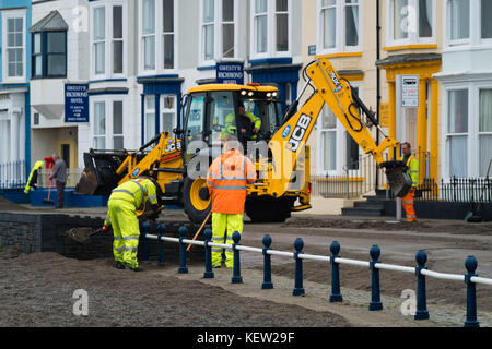 Aberystwyth Wales Vereinigtes Königreich, Montag, 23. Oktober 2017 Vereinigtes Königreich Wetter: Nach dem Sturm Wind und wilde Meere des Sturms Brian, Mitarbeiter des gemeinderats und Auftragnehmer, die JCB's und Bürsten verwenden, beginnen mit der Reinigung der Hunderte Tonnen von Sandsand und Kies, die an der Promenade und am Meer in Aberystwyth an der Küste von Cardigan Bay in westwales angespült wurden. Sie erwarten, dass die Straße bis zum Nachmittag wieder für den Verkehr freigegeben wird. Foto: Keith Morris/Alamy Live News Stockfoto