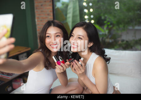 Zwei asiatische Frauen im Schlafzimmer auf dem Bett malen ihre Nägel und Spaß haben Stockfoto