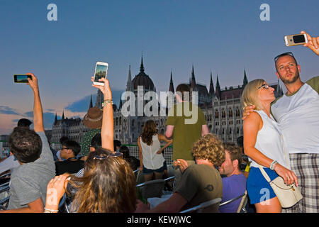 Horizontale Ansicht von Touristen an einem Abend Fluss Kreuzfahrt Fotos der Häuser im Budapester Parlament. Stockfoto