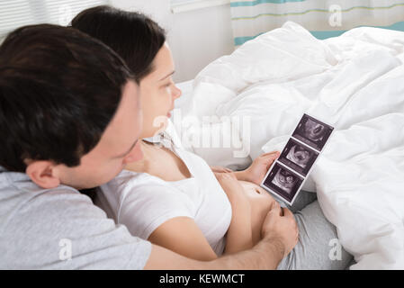 Junges Paar an Ultraschall auf der Suche Scan Ihrer erwarten Baby zu Hause Stockfoto